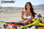 Risk Racing's March Moto Model Amber Juliana wearing a white bikini standing behind a motocross bike resting her crossed hands on the seat - close up shot - white fenced off MX track in background