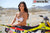 Risk Racing's March Moto Model Amber Juliana wearing a white bikini behind a motocross bike - close up shot - white fenced off MX track in background