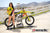 Risk Racing's March Moto Model Amber Juliana wearing a Yellow and Red VENTilate V2 Jersey and white bikini bottoms pulling up the Jersey on one side exposing her hip white posing in front of a motocross bike that's sitting on an ATS stand - wide shot - white fenced off MX track in background