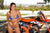 Risk Racing's May Moto Model Natalie Nicole wearing a 2 piece bikini posing in front of a motocross bike. Gripping her left pointer finger in her right hand. - close up shot - white fenced off MX track in background