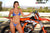 Risk Racing's May Moto Model Natalie Nicole wearing a 2 piece bikini posing in front of a motocross bike. Left hand on the throttle and right lightly touching her right thigh. - close up shot - white fenced off MX track in background