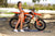 Risk Racing's May Moto Model Natalie Nicole wearing a 2 piece bikini posing sideways in front of a motocross bike that's sitting on an ATS Stand and Factory Pit mat by Risk Racing. She on her tip toes with left hand on the seat and right lightly touching her belly. Turning her buns more towards camera - wide shot - white fenced off MX track in background