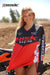 June Moto Model Rochelle Roche wearing a Risk Racing Factory Pit Dry-Fit Shirt. She's standing in front of an orange dirt bike. MX track in the background. Pose #5