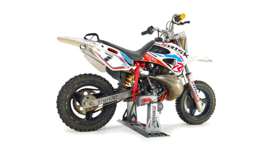 Youth dirt bike secured into a lock-n-load pro mini by Risk Racing on a white studio background.