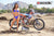 February Moto Model Alliyah wearing a blue bikini standing in front of a KTM dirt bike sitting on a Risk Racing ATS MX stand. At a MX track with mountains in background.