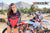 February Moto Model Alliyah tugging her Risk Racing Red & Black MX Jersey down over her bikini bottom standing in front of a KTM dirt bikeat a MX track with mountains in background.