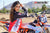 Close up shot of February Moto Model Alliyah wearing a Red & Black Risk Racing Jersey bare thigh below standing side profile in front of a KTM dirt bike #277 at a MX track with mountains in background. Right elbow resting on a handle bar grip