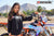 Close up of February Moto Model Alliyah wearing a Black Risk Racing Hoodie bare legs below standing in front of a KTM dirt bike #277 at a MX track with mountains in background.
