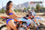 Close up of Risk Racing's February Moto Model Alliyah standing 3/4 pose away from camera showing the back of her blue bikini standing in front of a KTM dirt bike #277 at a MX track with mountains in background.