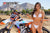 Risk Racing's February Moto Model Alliyah wearing a bikini standing in front of a KTM dirt bike number plate 277 with her hand grabbing a handle bar grip. At a MX track with mountains in background.