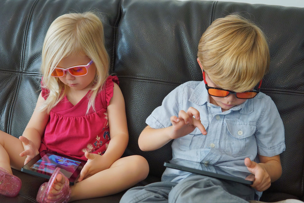 Two Children Using Digital Devices and Wearing Blue Light Blocker Glasses