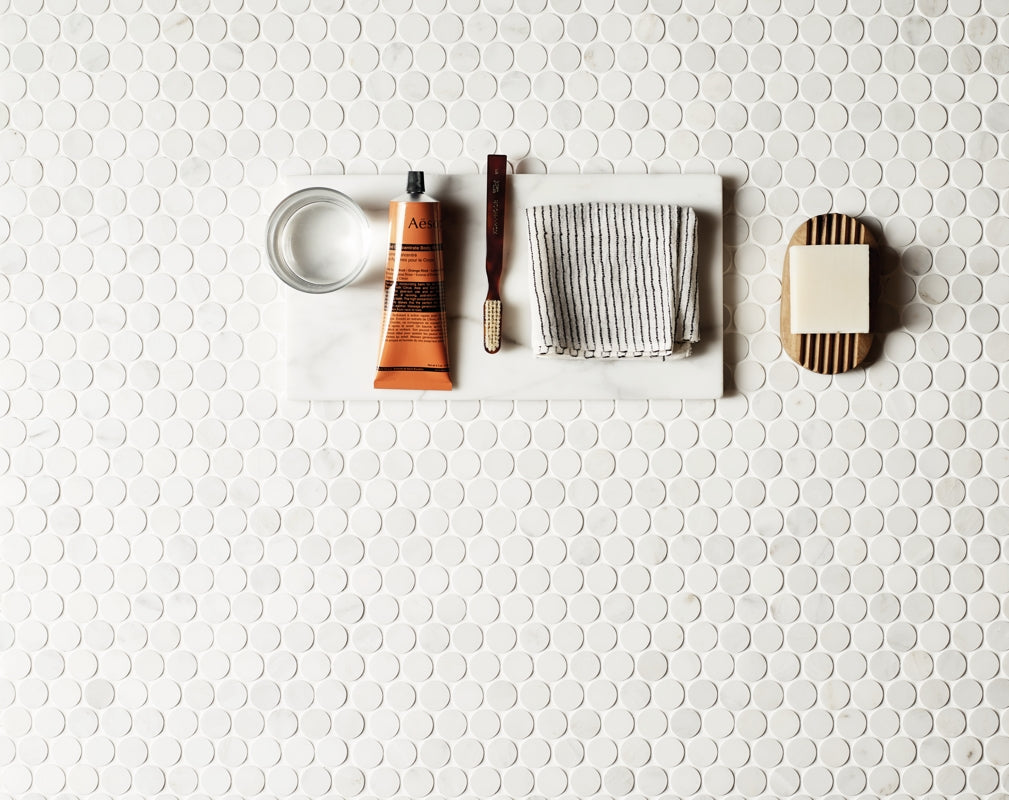 Bathroom accessories sit against a background of East Haven Penny Round Mosaic tiles by Claybrook Studio