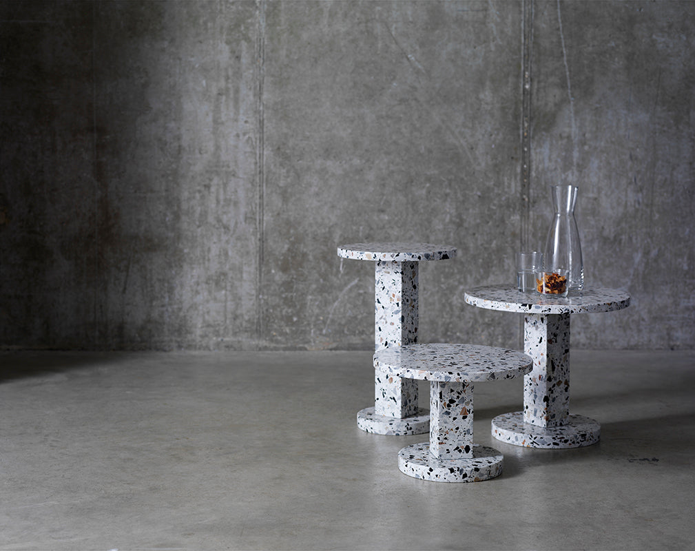 Three polished terrazzo side tables against concrete wall.