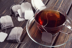 Tea bags with strings inside of a glass teacup.