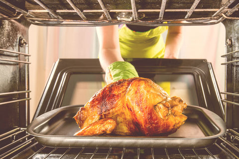 Hand putting baked chicken in the oven