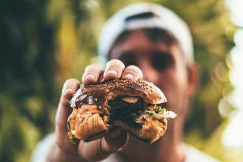 Closeup of a man holding a burger that he has bitten out of