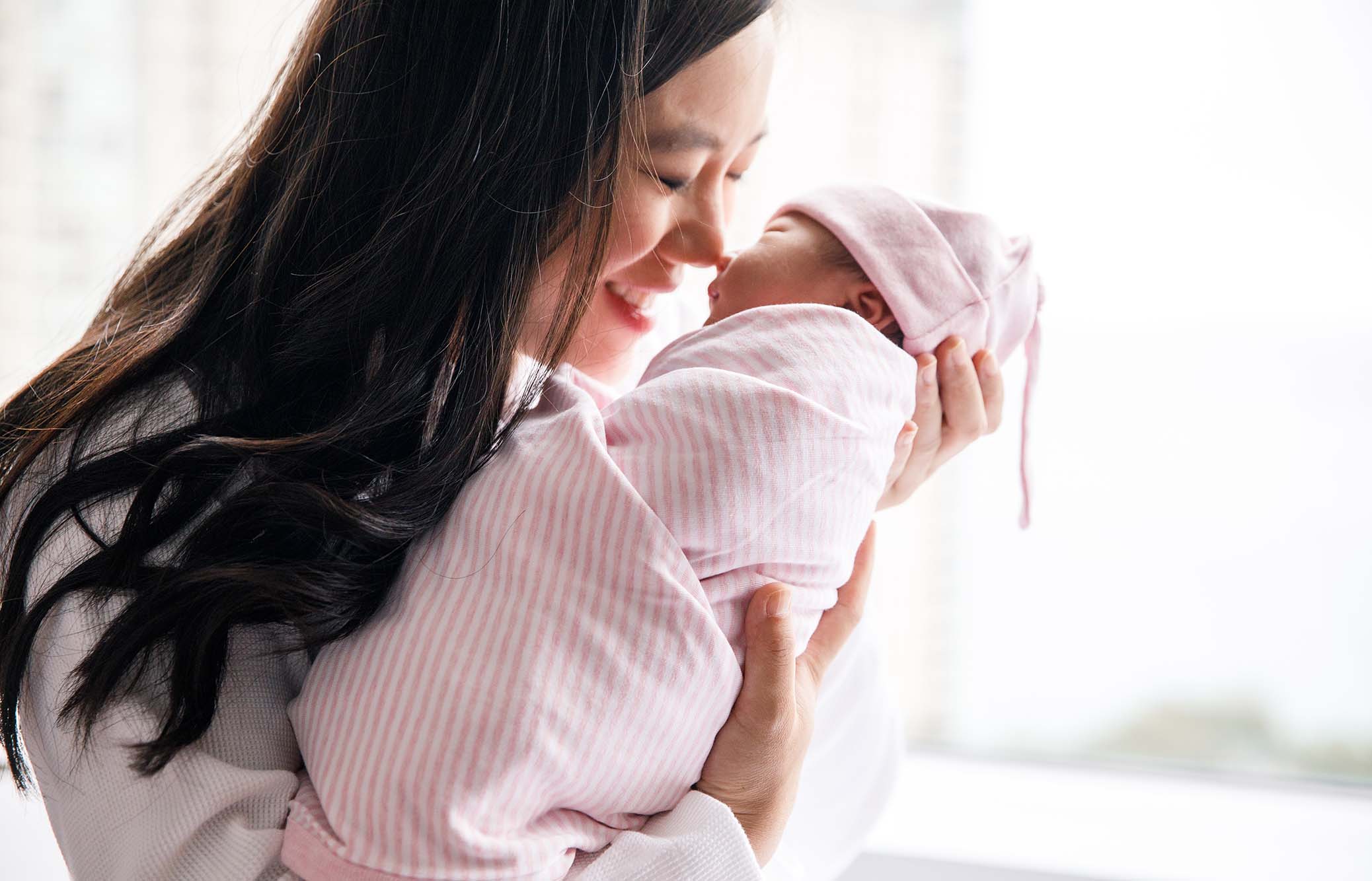 Mother holding swaddled newborn in pink