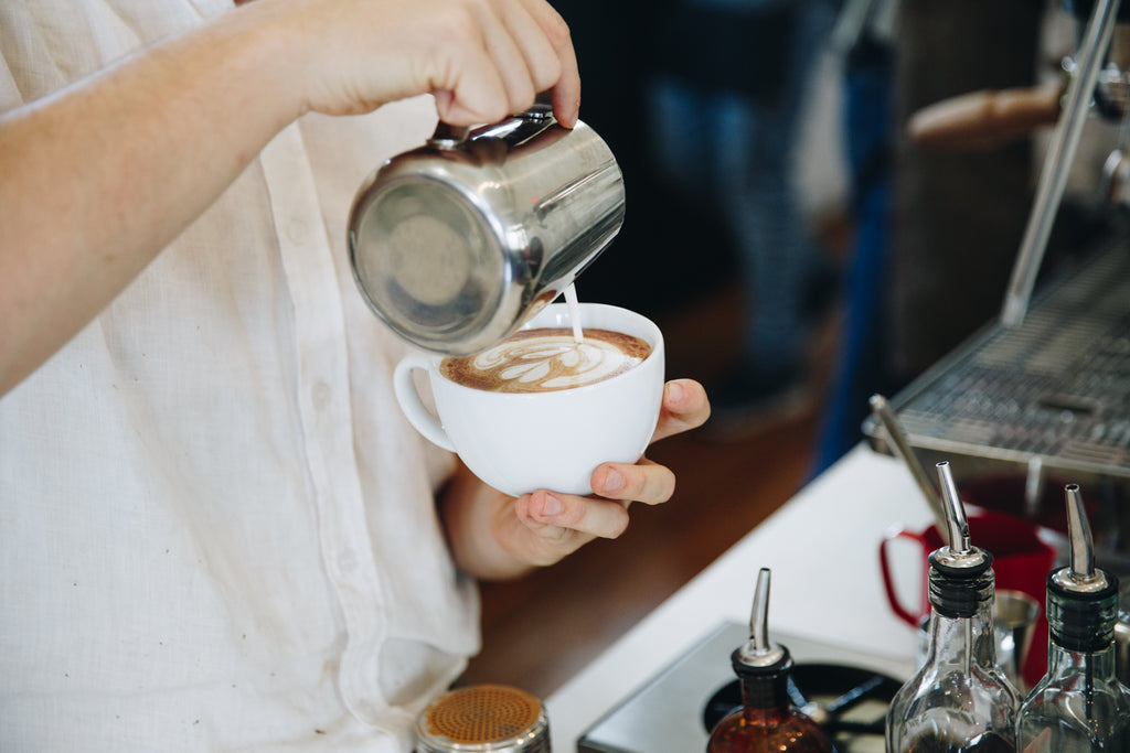 A close up photograph of a barista pouring an espresso based milk drink.