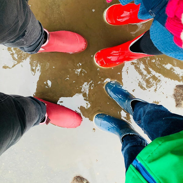 family wearing gumboots and standing in a puddle, two kids, one adult