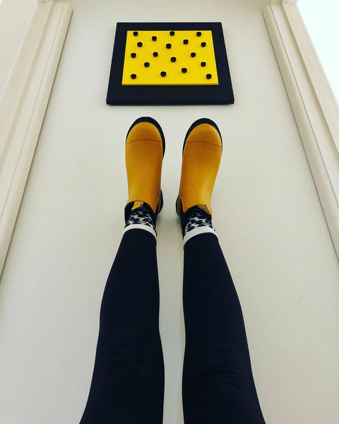 women wearing merry people yellow boots, legs leaning up against a wall