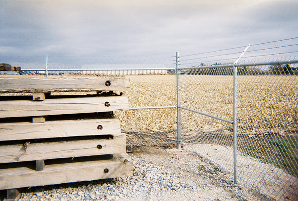 Some wood pallets stacked in front of the corner of a commercial chain link fence with barb wire running across the top