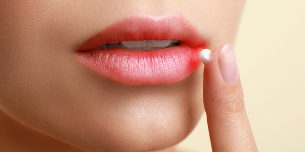 A woman with an early cold sore symptom, treating her lip with Blister Balm® External Analgesic Ointment.