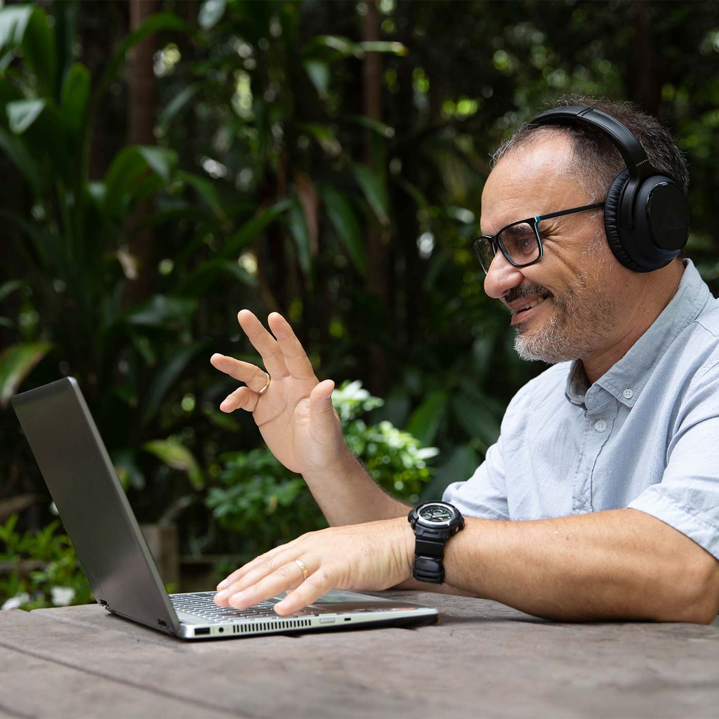 A man sitting at an outdoor table, wearing his Audeara headphones to join a virtual meeting on his laptop