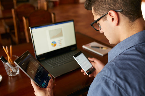 Man at laptop distracted by phone and tablet