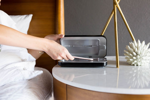 A woman places a phone into a PhoneSoap next to her bed
