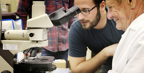 Wes and a scientist look into a microscope