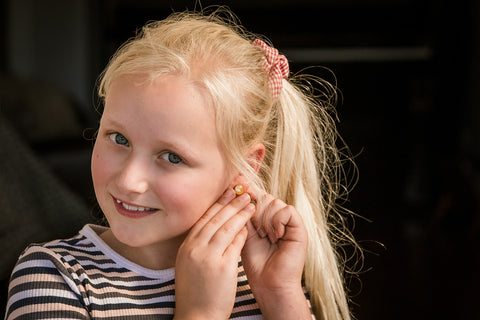 Image of a girl with a big smile, touching her ear lobes. She's happy because she is wearing the earrings she created herself.