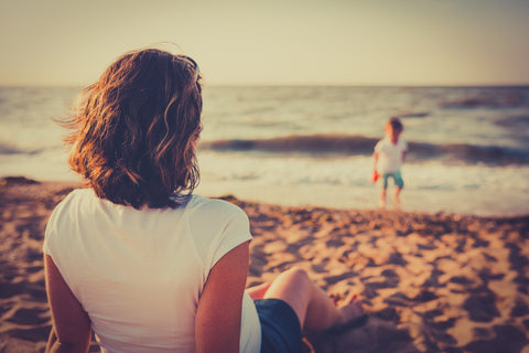 Parent sits back on a beach to watch her child play freely - Slow Parenting