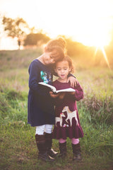 Two little girls enjoy reading in nature - a key value of Snail Mail Stories, inspiring literacy through nature