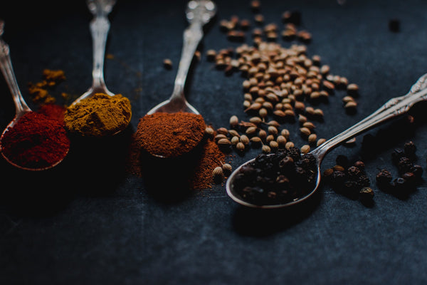 How Ayurveda is useful in modern life. An image of some silver spoons containing powdered herbs in various colours. There are some legumes scattered on the table beside the spoons.   