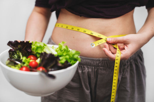 Woman holding a bowl of healthy salad and measuring her waist