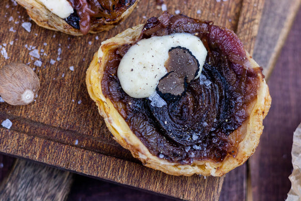 Puff pastry filled with caramelized onion with black truffle tarte tatin on cutting board
