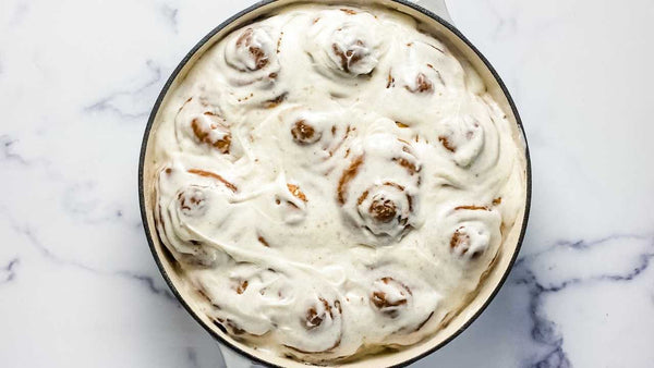 orange and turmeric sweet rolls in a skillet with a black tea cream cheese frosting on top