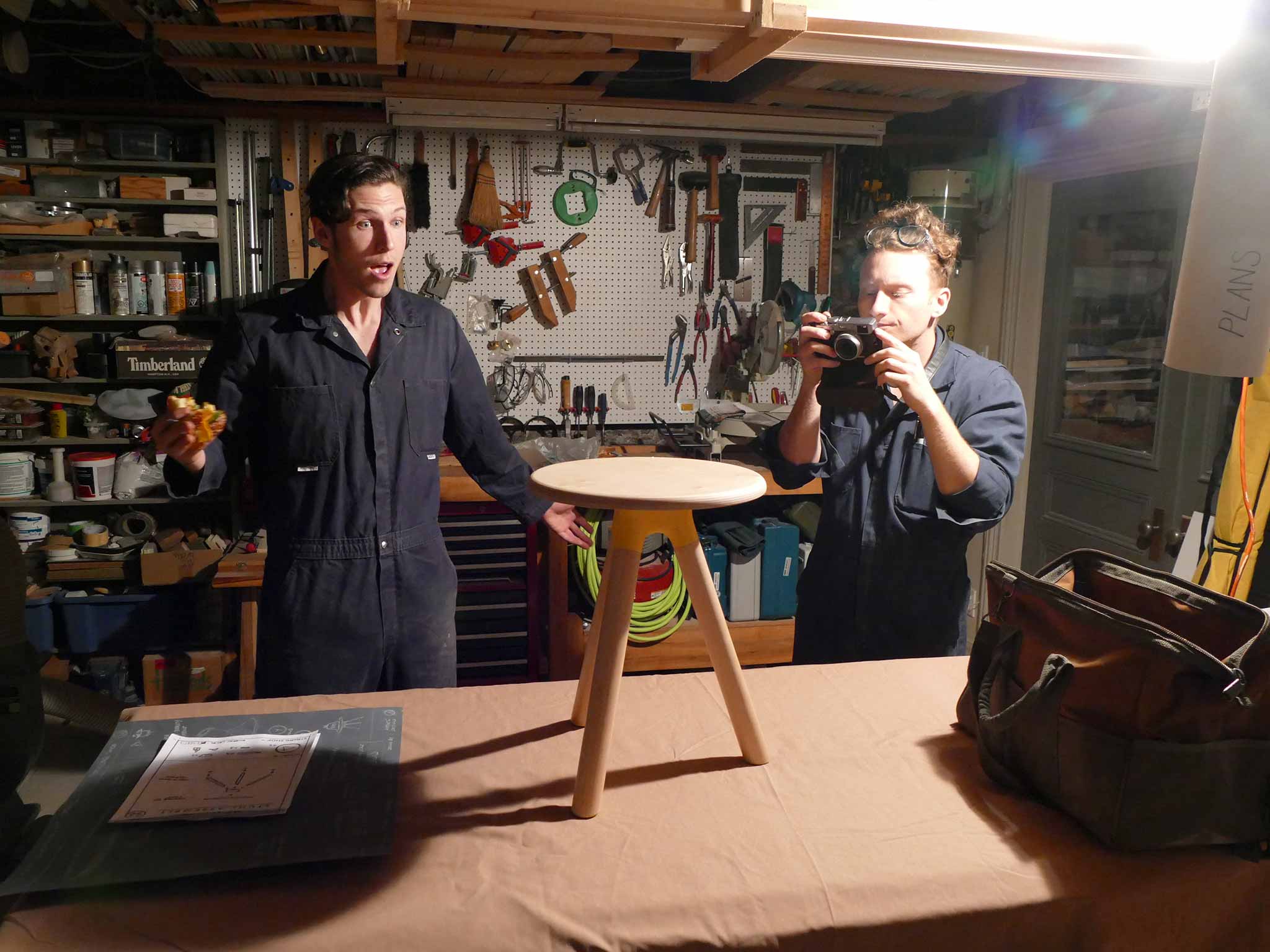 Two-Workers Look at a Finished Stuhl-Stool and Photograph it While One Worker Eats a Sandwich