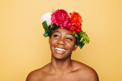 Woman of color in front of yello background with floral crown on her head