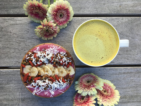smoothie bowl with daisies and a golden latte, on wood background 