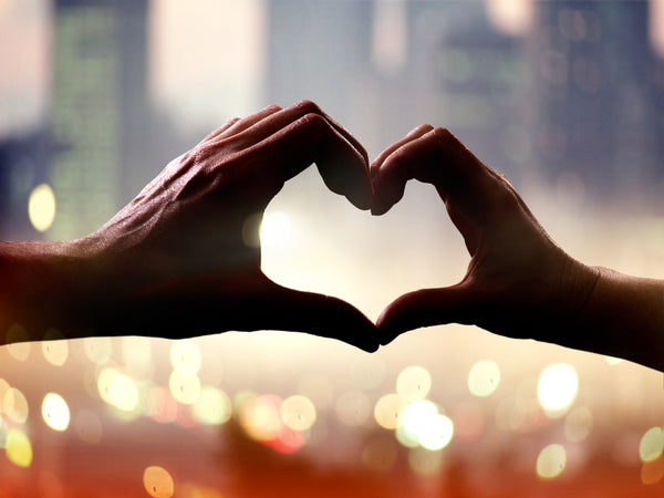 hands making heart shape with flickering candles in background