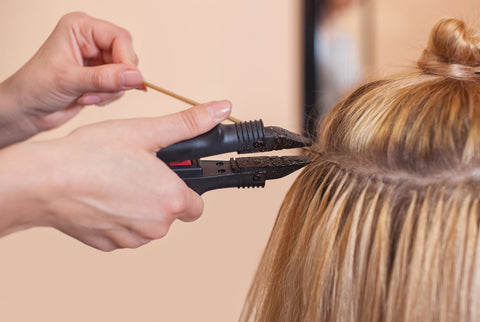 blonde woman having keratin fusion extensions installed by a stylist