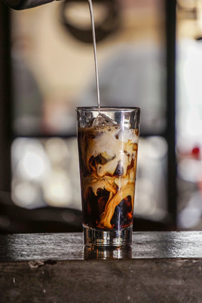 a stream of milk is poured into glass of iced coffee