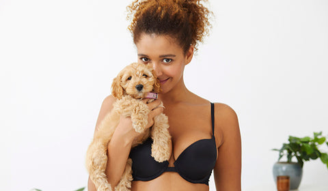 Woman wearing black bra, holding puppy