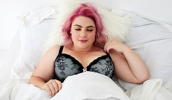 Woman wearing bra in bed with covers pulled up to chest