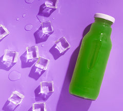 a bottle of matcha green tea on a purple background next to scattered ice cubes
