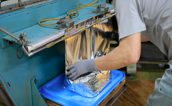 Warehouse worker bundles a package of bulk matcha powder in silver foil wrap.