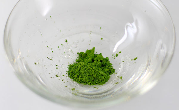 A small amount of bulk matcha powder in a small glass bowl.
