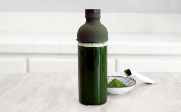 A glass water bottle full of green tea made from matcha to-go packets.