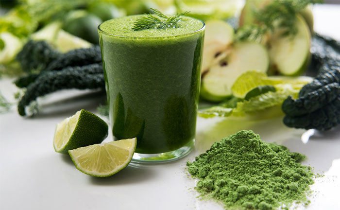 A glass of matcha green tea next to other green fruits and vegetables.